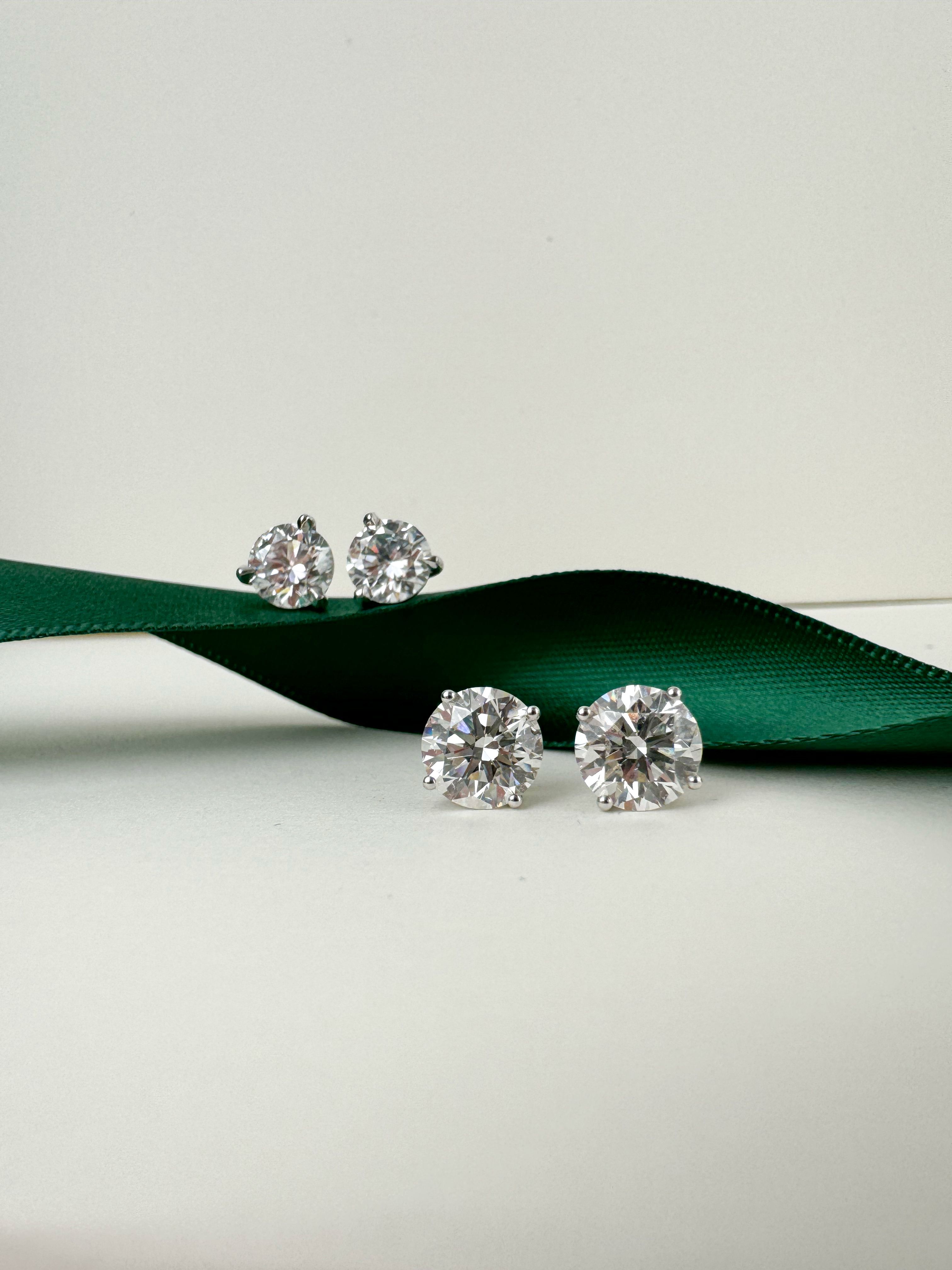 Image of two pairs of round diamond studs on a dark green ribbon