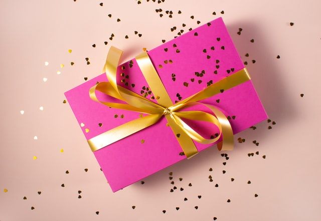 pink gift box wrapped with gold ribbon and confetti 