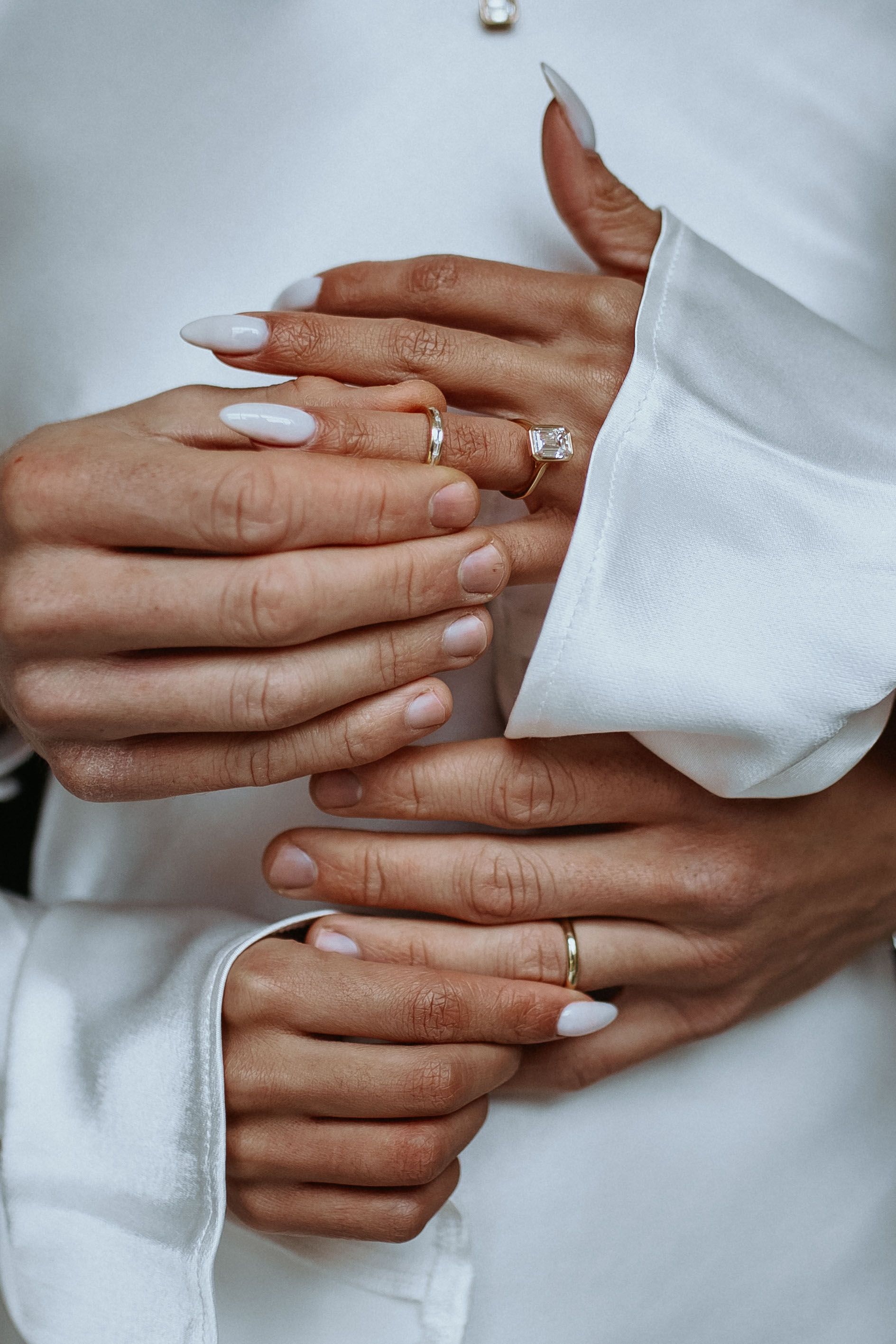 Image of a couple's hands wearing an engagement ring and wedding bands